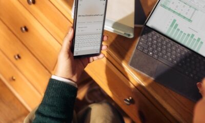 Person holding phone near laptop and tablet on desk