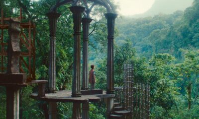 a white woman with dark curly hair standing in a beautiful architectural structure in a forest