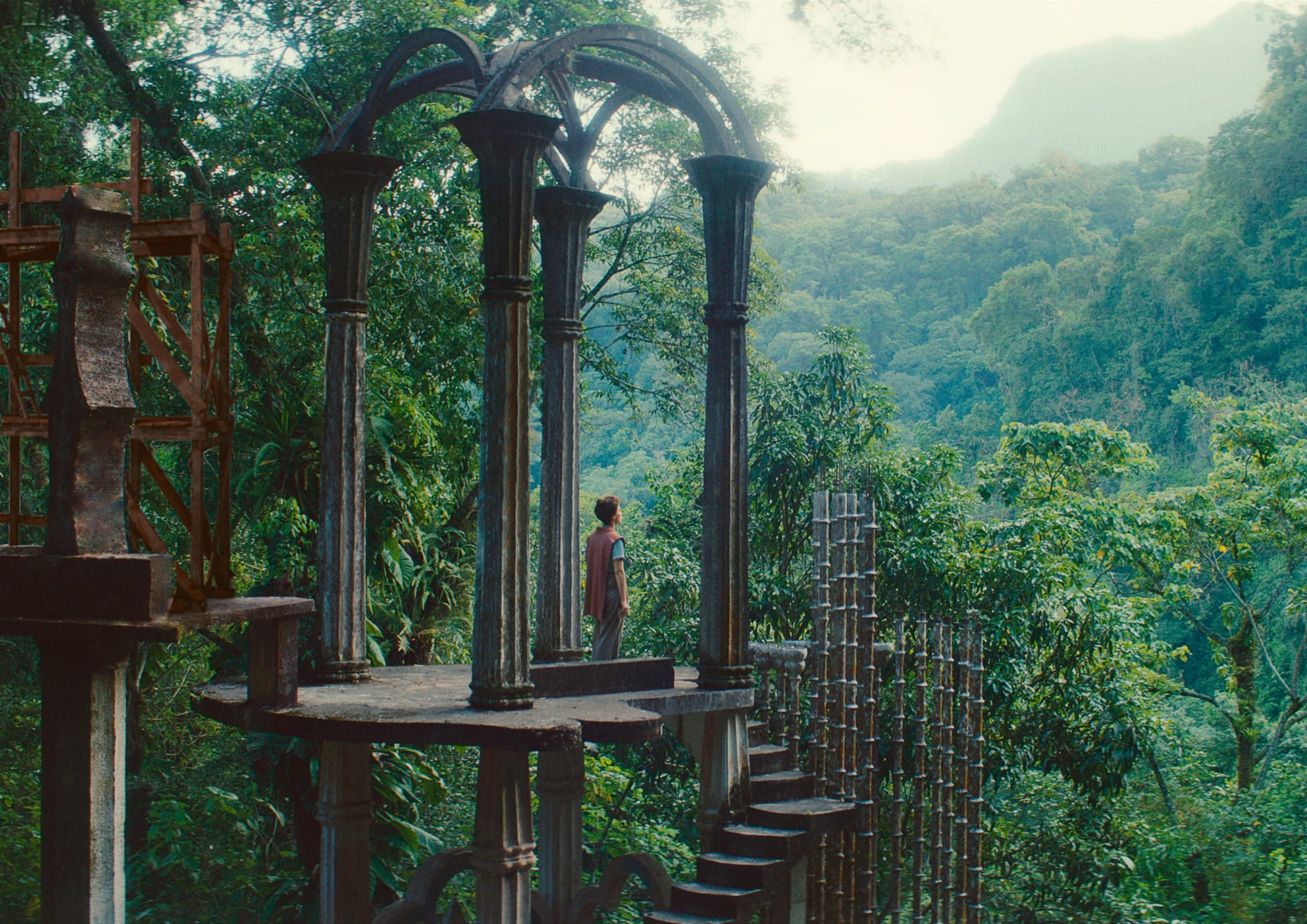 a white woman with dark curly hair standing in a beautiful architectural structure in a forest